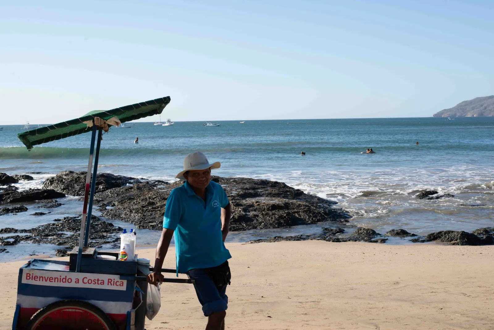 A vendor with a cart on the beach at Tamarindo, boats moored offshore